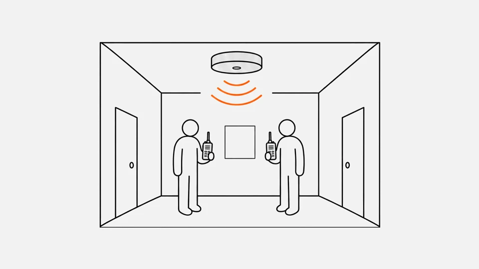 Two people with handheld radios in a corridor under a ceiling Wi-Fi access point